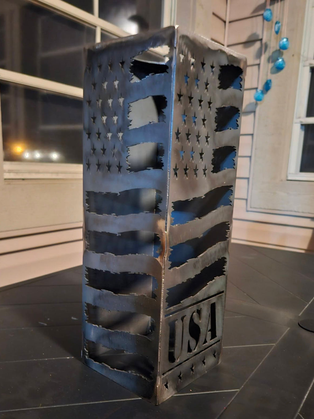 A rustic metal decorative lantern with a cutout American flag pattern and 'USA' embossed on the front.